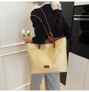 Detail of a beige woven straw tote bag with brown leather handles and shoulder knot