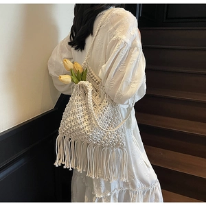 Detailed view of white crochet tassel bag with long fringes on dark wood stairs