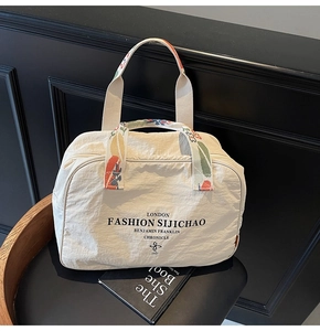 Detail of cream nylon travel bag featuring floral embroidery on handles and large capacity