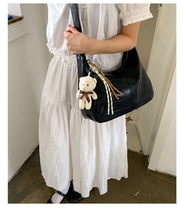 Detail of black crocodile texture shoulder bag with cute cream bear charm and fringe