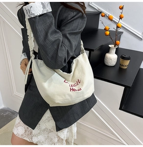 Detail of off-white canvas crossbody bag with pleated strap and red letter embroidery