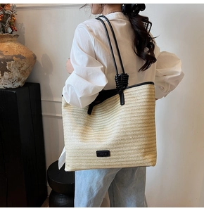 Detailed view of straw tote bag showing fine woven texture and black leather shoulder strap