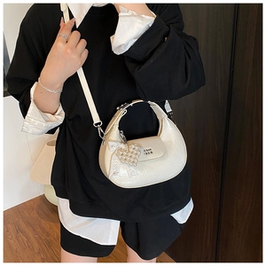 Close-up of white crescent crossbody bag with pearl lace bow charm and leather texture