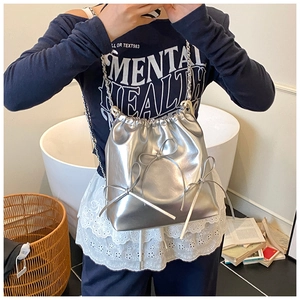 Detail of silver drawstring bucket bag with decorative bows and metallic chain strap