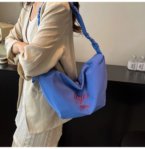 Blue nylon tote bag with pleated shoulder strap and red text logo shown on a model