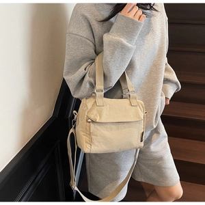 Detail of a lightweight beige nylon crossbody bag with front zipper pocket and adjustable strap