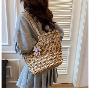 Detail of woven straw tote bag with purple butterfly charm worn by a model