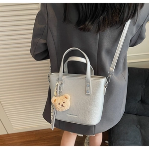Silver bucket bag with litchi texture shown on a model with a cute bear charm and scarf