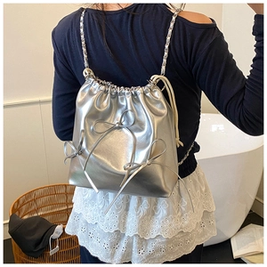 Detail of metallic silver bucket bag featuring ribbon bows and chain straps on model