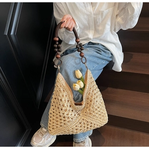 Detail of hand-woven straw tote with hollow pattern and beaded wooden handle strap