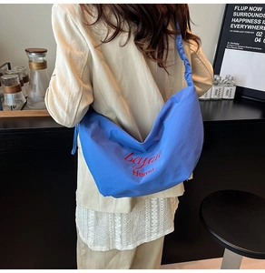 Detailed back view of a royal blue crescent bag with red text and pleated strap