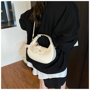 Detail view of cream white half-moon bag with pearl lace bow charm on model