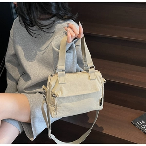 Detailed view of a lightweight beige nylon crossbody bag held by a casual model