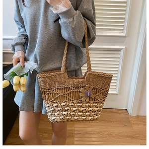 Detailed close-up of woven straw tote bag with textured patterns and flower pendant