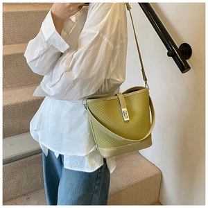 Detail view of a woven green bucket bag with a golden lock worn by a model in a casual outfit