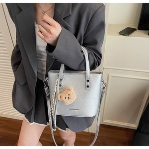 Close-up of silver lychee grain leather handbag with plush bear charm detail