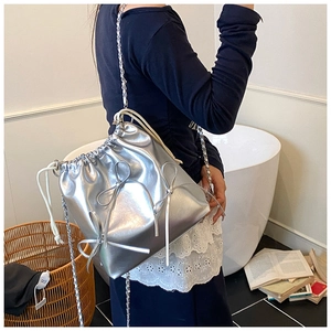 Detail of silver metallic drawstring bucket bag with bow accents and chain strap
