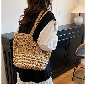 Detail of hand-woven straw tote bag with purple floral accent worn on the shoulder