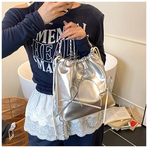 Close-up of shiny silver metallic bucket bag with 3D bow and elegant chain strap