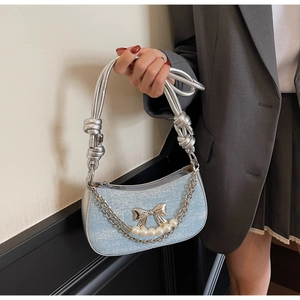 Close-up of denim texture bag with silver bow, pearl chain and knotted shoulder strap
