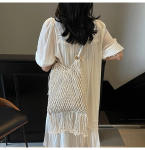 Detail of white crochet bucket bag featuring long tassels and wooden handle rings