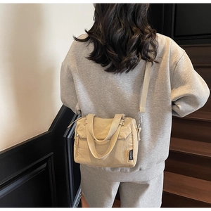Rear view of model wearing a beige nylon shoulder bag with adjustable strap on stairs