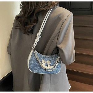 Detail of blue denim underarm bag with silver bows, chains, and large pearl decorations