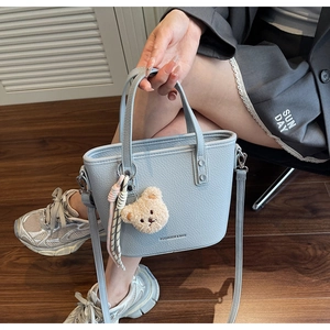 Detail of light blue lychee pattern bucket bag with plush bear charm on model