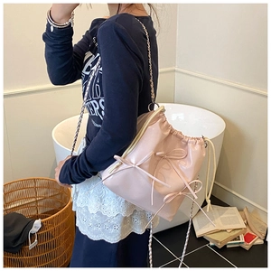 Detail of pink drawstring bucket bag with decorative bows and chain strap worn by model
