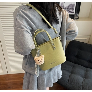 Green leather bucket bag with bear pendant shown on a sofa in a modern lifestyle setting