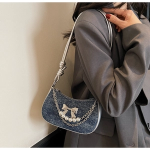 Detail of blue denim underarm bag with silver bow, pearls and metal chain on model
