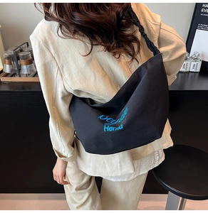 Detail of black canvas tote bag with blue print and pleated shoulder strap on model