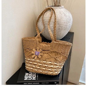 Detail of woven straw tote bag featuring purple butterfly floral charm and mesh pattern