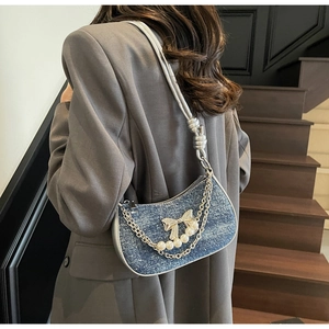 Detailed view of blue denim underarm bag with crystal bow and pearl chain decoration