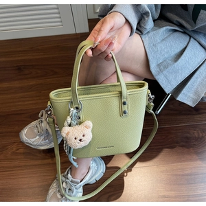 Detail view of light green bucket bag in pebble leather with a cute bear charm