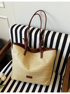 Minimalist beige woven tote bag with dark brown leather straps on striped chair