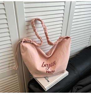 Detailed view of pink canvas tote bag featuring soft pleated shoulder straps and text print