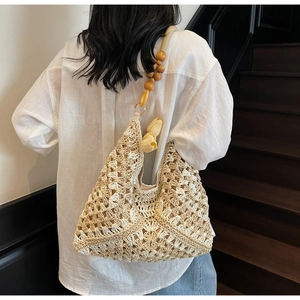 Detail of hand-woven beige straw hobo bag featuring a wooden bead strap and tulip charm
