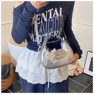Detail of silver metallic pleated crescent bag with pearl heart and lace bow accent
