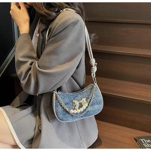 Detail of blue denim shoulder bag featuring pearl bow and chain on gray blazer