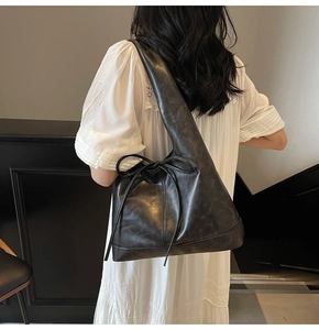 Détail du sac à bandoulière en cuir noir brillant avec un ruban décoratif sur le côté