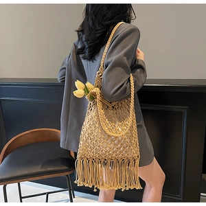 Side view of beige woven tote bag with long tassels used as a shoulder bag