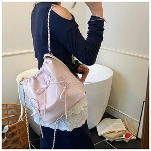 Pink drawstring bucket bag with decorative bows and metallic chain strap on model