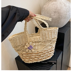 Detail of hand-woven straw tote bag with floral charm and purple butterfly accent