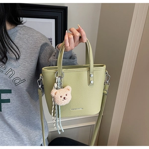 Close-up of light green lychee texture handbag with a cute plush bear charm accessory