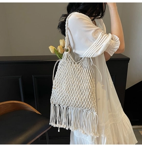 Detail of white bohemian woven bucket bag with long tassels and wooden handle