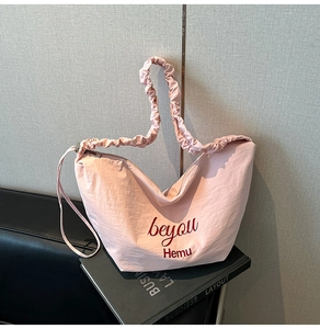Detailed view of pink crescent canvas tote with pleated shoulder strap and red text print