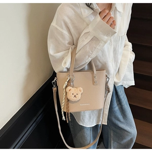Beige leather bucket bag detail with plush bear charm and adjustable shoulder strap