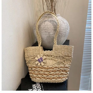 Close-up of woven straw tote bag featuring purple flower charm and beige contrast stitching