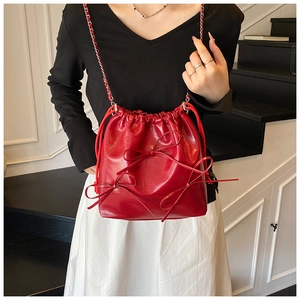 Detail of red bucket bag with bow accents and chain strap shown on a model